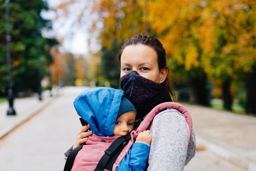 Woman with face mask carries child